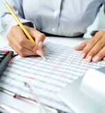 Photo of human hands holding pencil and ticking data in documents